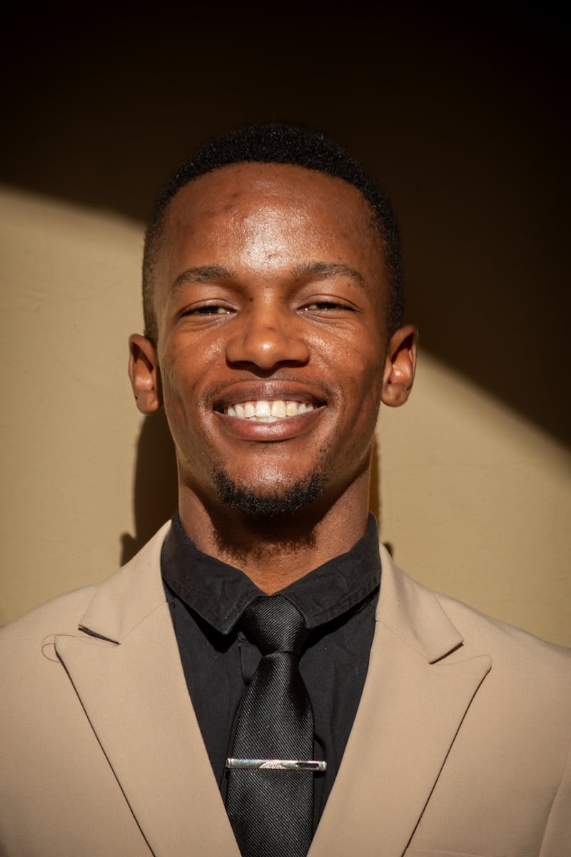 Portrait of a smiling man in a beige suit and black shirt, highlighting elegance.