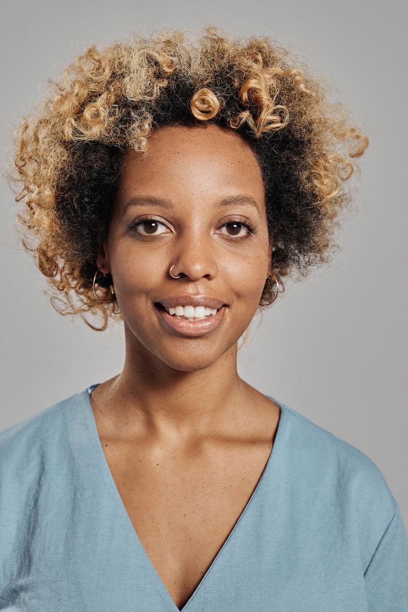 Close-up portrait of a happy woman with curly hair and a nose ring against a gray background.