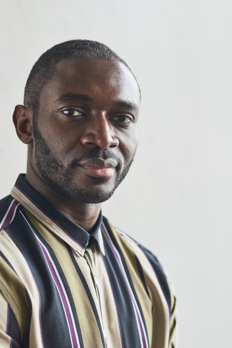 Close-up portrait of a confident man with a beard in a striped shirt, indoors.